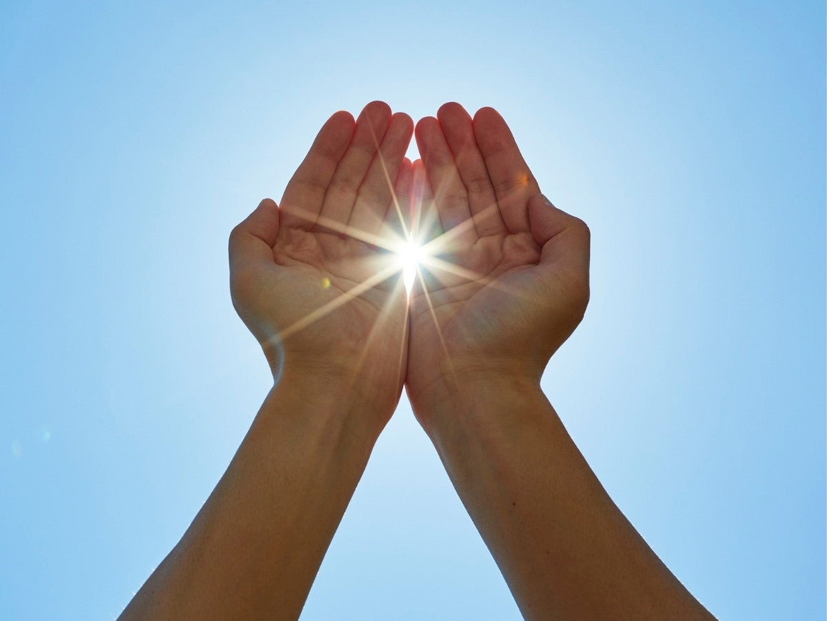 person with arms outstretched getting vitamin d from the sun blue sky in the background