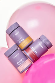 Three purple supplement bottles with different labels on a pink background