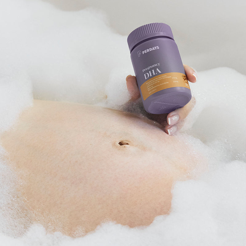 Person holding a bottle of Perdays Pregnancy DHA while lying in a bubble bath.