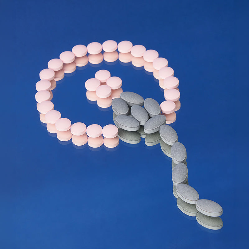 Pink and gray oval-shaped pills arranged in a sperm shape on a blue background