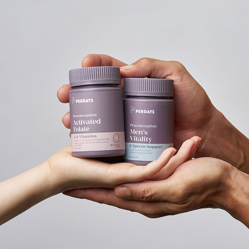 Two hands holding Perdays vitamins against a gray background